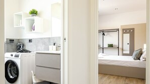 A compact room with a washing machine, a small sink, and a bed.