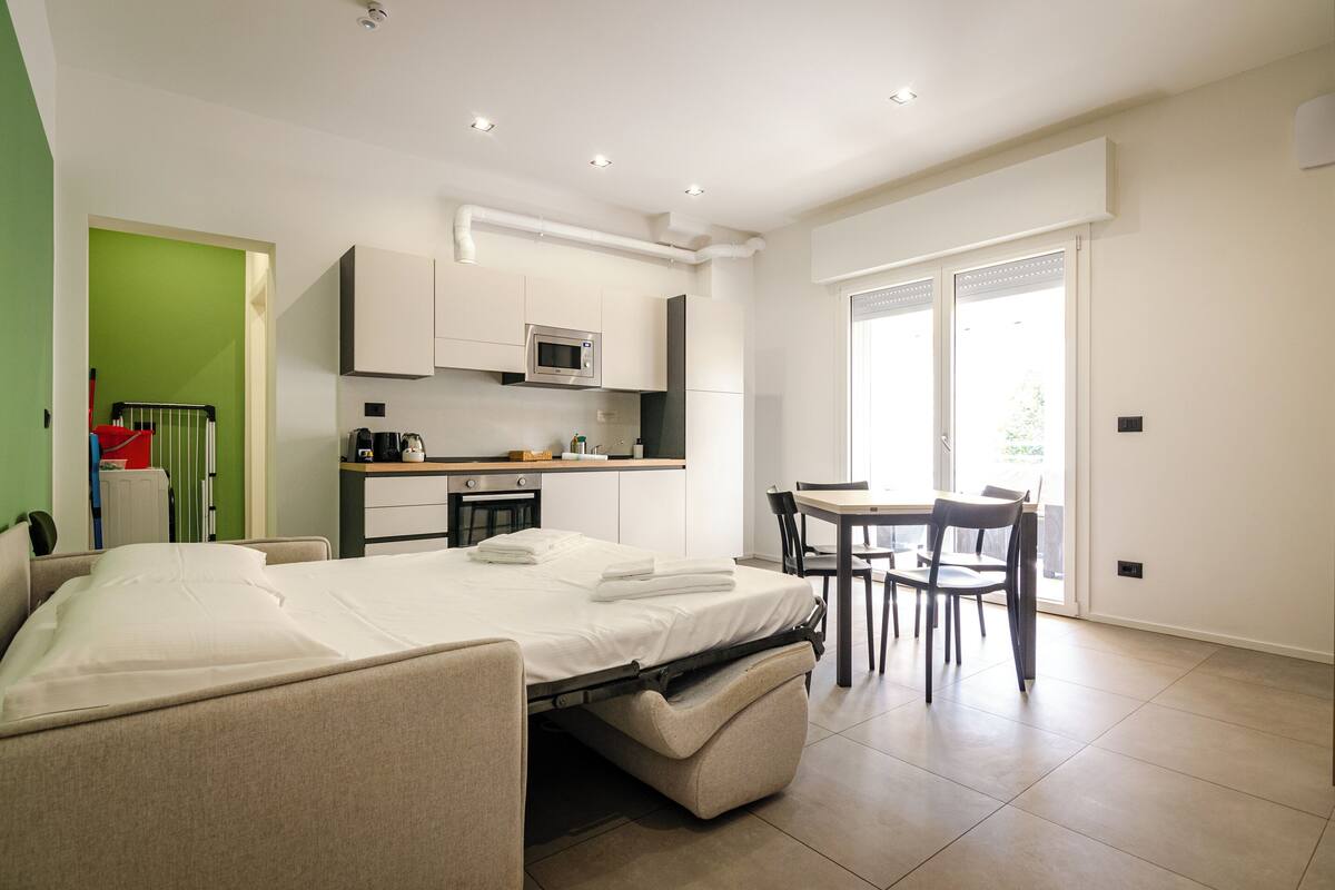 A modern room with a bed, kitchenette, dining area, and a sliding glass door.