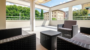A covered outdoor seating area with wicker furniture and a view of buildings and trees.