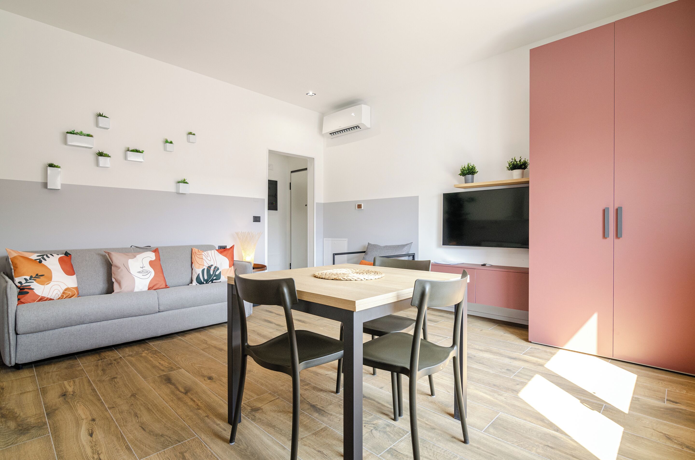 A modern living room with a sofa, dining table, chairs, a flat-screen TV, and a pink cabinet.