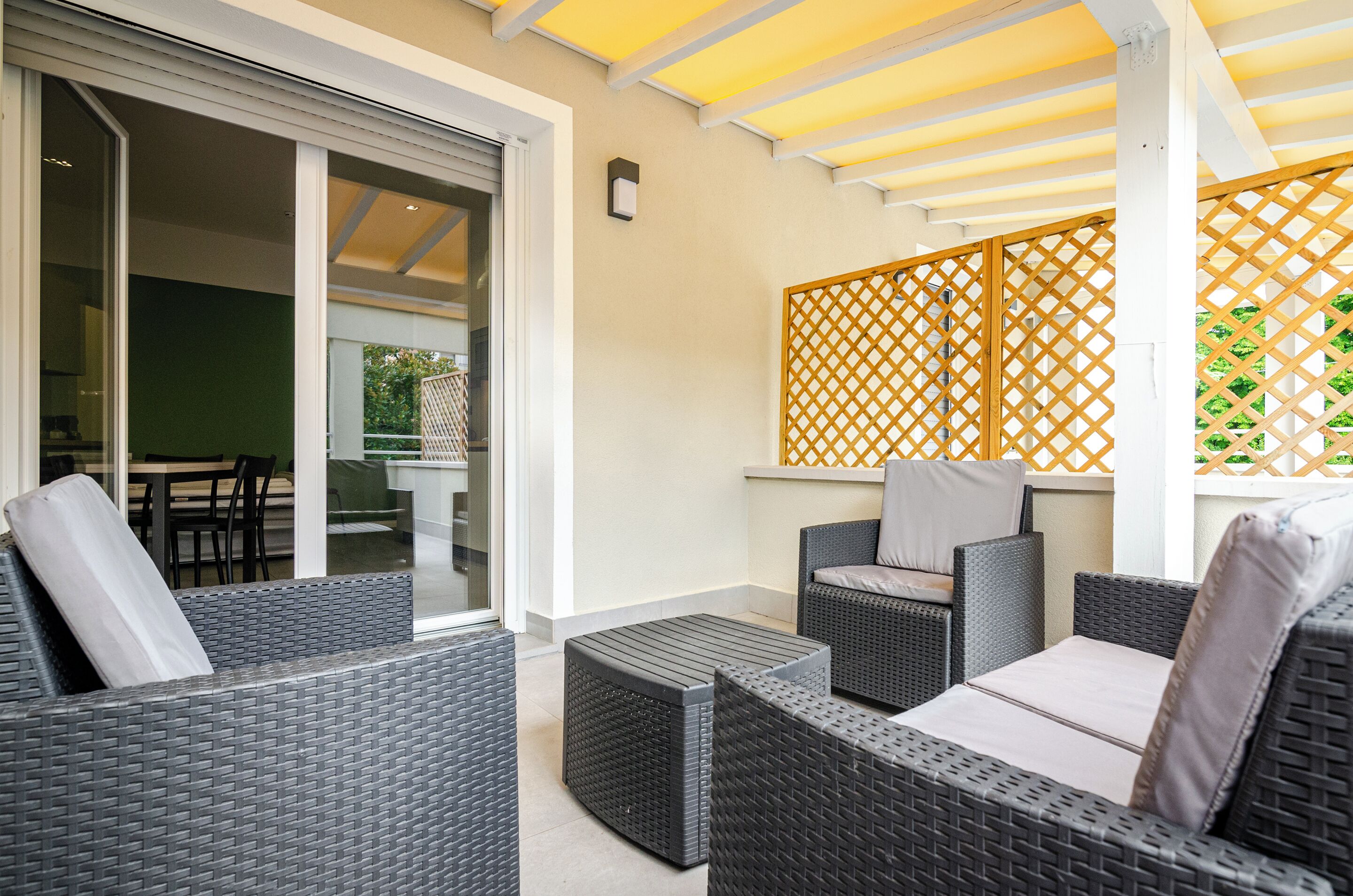 A covered outdoor seating area with wicker furniture and a sliding glass door leading to an indoor space.
