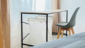 A small room with a bed, a desk with a chair, and a window with sheer curtains. - Central spacious apartment with roof terrace! (Bochum)