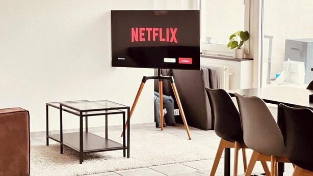 A modern living room with a flat-screen TV displaying 'NETFLIX,' a glass coffee table, a brown leather chair, and a dining area with black chairs. - Central spacious apartment with roof terrace! (Bochum)