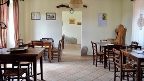 A dining area with wooden tables and chairs, a woven ceiling light, and a stone wall. - Room in typical farmhouse, nestled in the green hills of Gubbio (Gubbio)