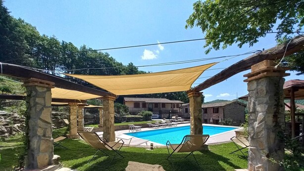 A pool area with stone pillars, a covered seating area, and a view of buildings in the background. - Room in typical farmhouse, nestled in the green hills of Gubbio (Gubbio)