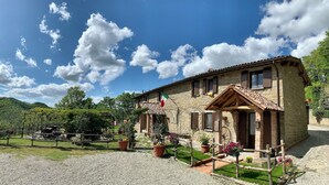 A stone building with a tiled roof, a flag, and a gravel driveway. - Room in typical farmhouse, nestled in the green hills of Gubbio (Gubbio)