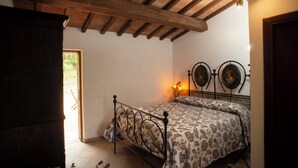 A bedroom with a wooden ceiling, a bed with a patterned bedspread, and two wall-mounted decorative plates. - Room in typical farmhouse, nestled in the green hills of Gubbio (Gubbio)