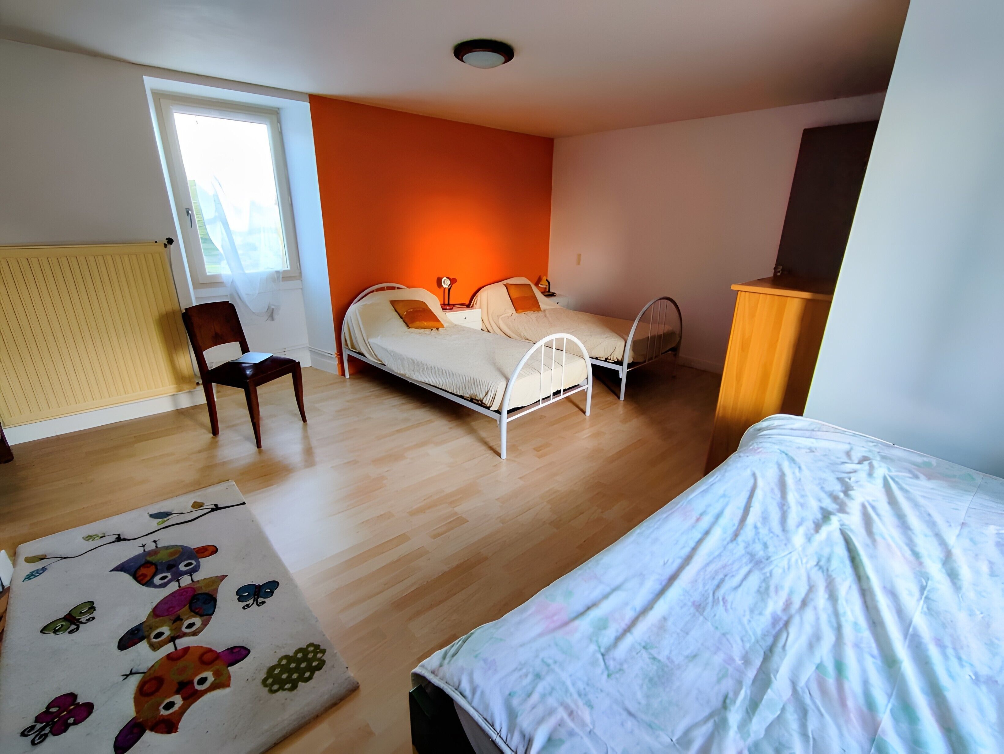 A bedroom with two beds, a chair, a radiator, and a window.