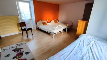 A bedroom with two beds, a chair, a radiator, and a window.