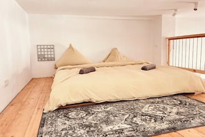 Quarto com cama, almofadas, tapete e janela.