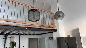 A loft-style room with a wooden balcony, pendant lighting, and a modern kitchen area.