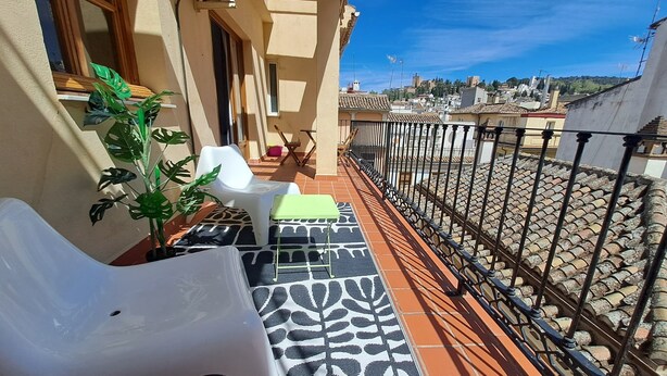 Un balcon avec un sol à motifs, une chaise blanche, une table verte et une plante en pot.