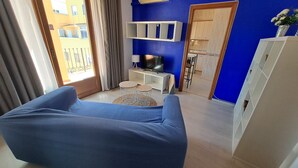 A living room with a blue sofa, a TV, a small round table, and a cabinet. - Nest Flats Navas (Granada)