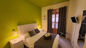 Une chambre d’hôtel avec un mur vert, un lit blanc, une table de chevet avec une lampe, une fenêtre avec des rideaux et un t éléviseur fixé au mur.