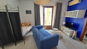 Une pièce comprenant un canapé, un téléviseur, une petite table, une lampe, une armoire et un panneau affichant des messages de bienvenue dans plusieurs langues.
