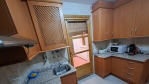A compact kitchen with a sink, stove, microwave, and wooden cabinets. - Nest Flats Navas (Granada)