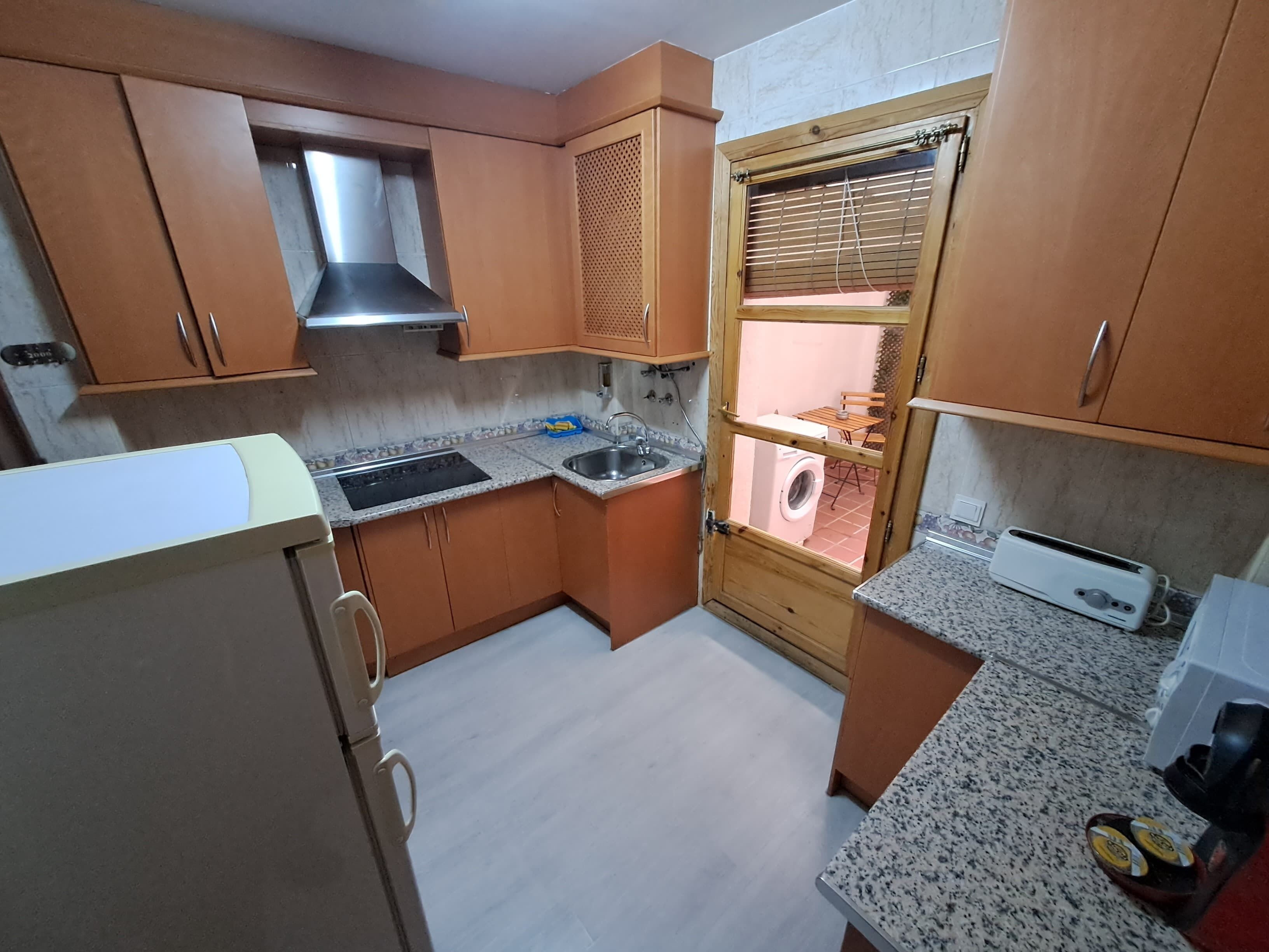 A compact kitchen with wooden cabinets, a built-in oven, a sink, and a window with blinds.
