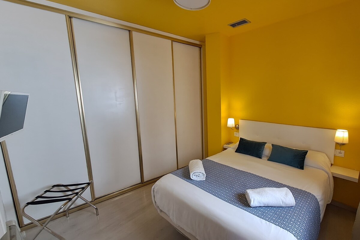 Ein Hotelzimmer mit einem Bett, Nachttischlampen, einem Fernseher und einem Kleiderschrank.