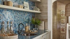 Cozinha com painel de azulejos azuis, armários brancos e piso de madeira.