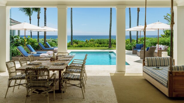 Uma área à beira da piscina com mesa e cadeiras, uma cadeira de balanço e vista para o oceano.