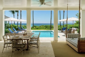 A poolside area with a table and chairs, a swing chair, and a view of the ocean.