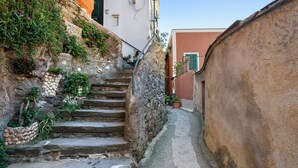 Un escalier étroit en pierre mène à un bâtiment à la façade blanche et aux volets verts.