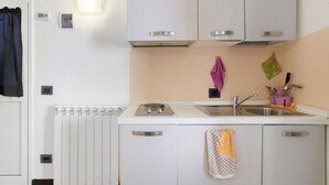 Une cuisine compacte avec un plan de travail blanc, un évier et une cuisinière intégrée. On y trouve des placards dotés de poignées et une serviette accrochée à l’un d’eux.