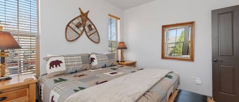 A bedroom with a bed, two bedside tables, a wall-mounted decorative item, a window, and a door.