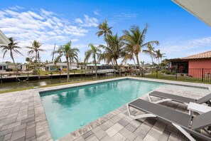 A swimming pool with lounge chairs, palm trees, and a clear sky. - Barefoot Escape (Fort Myers Beach)