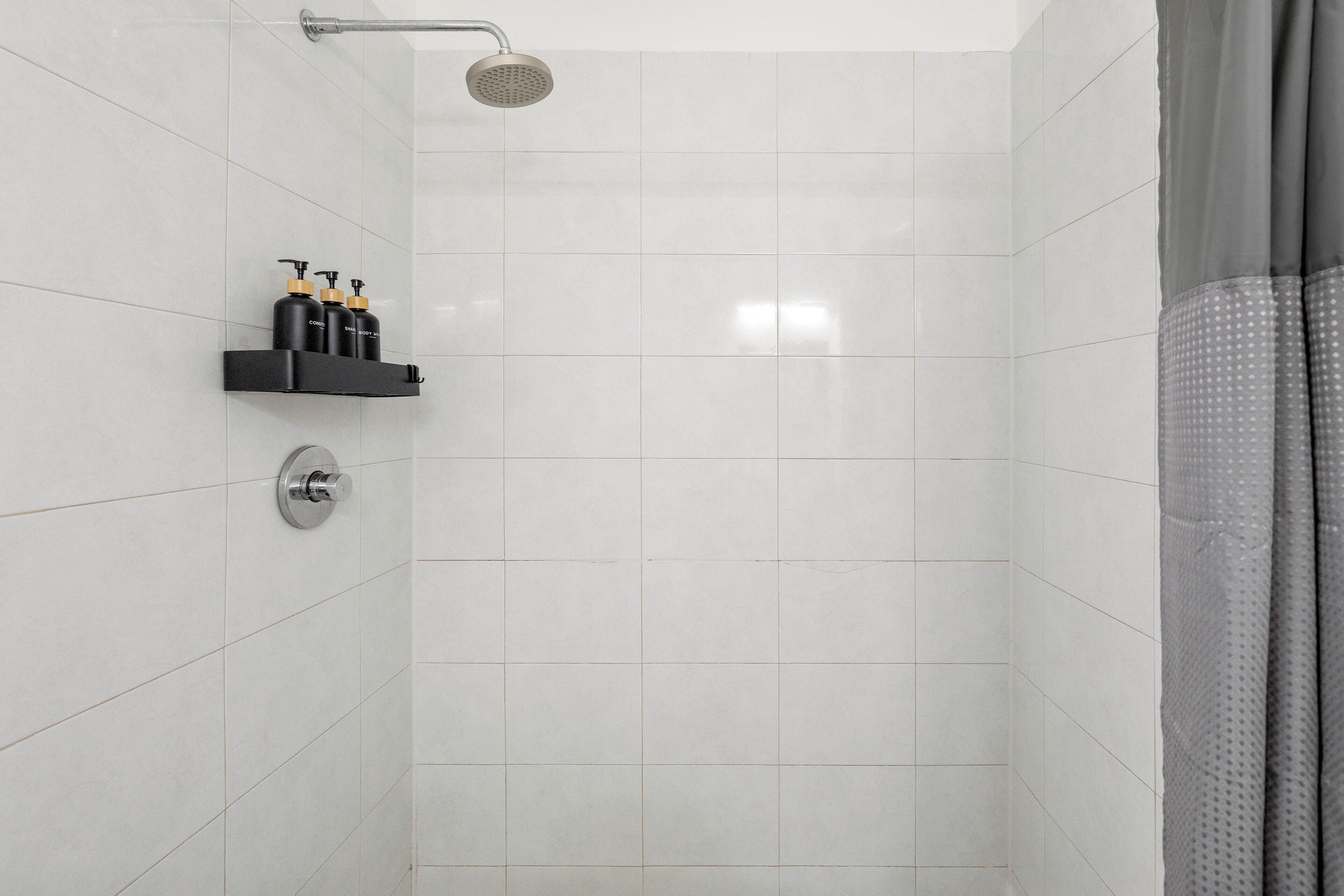 Een douche met een handdouche, een wandmengkraan en een plank met toiletartikelen.