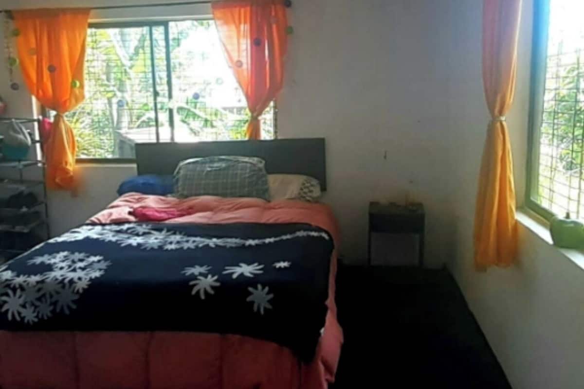 A bedroom with a bed, a window with curtains, a bedside table, and a view of greenery outside.