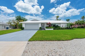 A single-story house with a garage, a well-maintained lawn, and a gravel driveway. - 🏖️Private Heated Pool | Canal Front | Gorgeous Views | Barefoot Escape🏖️ (Fort Myers Beach)
