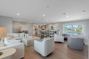 A modern living room with a sofa, armchairs, a coffee table, and a dining area with chairs and a table. - 🏖️Private Heated Pool | Canal Front | Gorgeous Views | Barefoot Escape🏖️ (Fort Myers Beach)