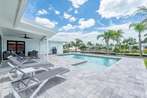 A swimming pool with lounge chairs, a ceiling fan, and a view of palm trees and houses. - 🏖️Private Heated Pool | Canal Front | Gorgeous Views | Barefoot Escape🏖️ (Fort Myers Beach)