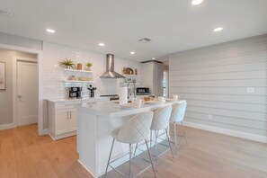 A modern kitchen with white cabinetry, a central island with bar stools, and a stainless steel range hood. - 🏖️Private Heated Pool | Canal Front | Gorgeous Views | Barefoot Escape🏖️ (Fort Myers Beach)