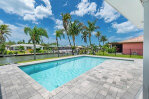A swimming pool with a tiled deck, surrounded by palm trees and a body of water. - 🏖️Private Heated Pool | Canal Front | Gorgeous Views | Barefoot Escape🏖️ (Fort Myers Beach)