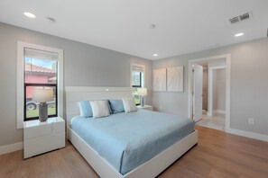 A bedroom with a bed, nightstands, a window with blinds, and a door leading to another room. - 🏖️Private Heated Pool | Canal Front | Gorgeous Views | Barefoot Escape🏖️ (Fort Myers Beach)