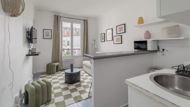 A compact kitchen with a checkered floor, a dining area with a sofa, and a window with a view of buildings. - Orleans  - Paris Neuilly 4Pax (Neuilly-sur-Seine)