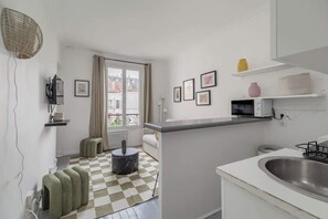 Eine kleine Küche mit Schachbrettboden, ein Essbereich mit einer Couch und ein Fenster mit Blick auf Gebäude.