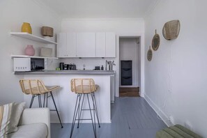 Une cuisine compacte avec des meubles blancs, un tabouret de bar et un coin repas agrémenté d’un canapé.