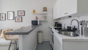 A compact kitchen with white cabinets, a stainless steel sink, a microwave, and a small trash can. - Orleans  - Paris Neuilly 4Pax (Neuilly-sur-Seine)