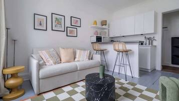 A modern living room with a sofa, a coffee table, and a kitchen area with white cabinets and a bar stool.