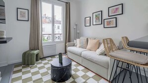 A modern living room with a sofa, two wicker chairs, a checkered floor, a black marble table, and artwork on the walls. - Orleans  - Paris Neuilly 4Pax (Neuilly-sur-Seine)