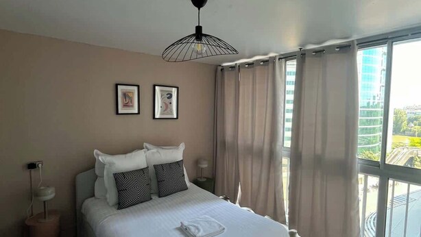 Une chambre avec un grand lit, une table de chevet, un luminaire suspendu et une vue sur l’extérieur.