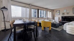 Un salon moderne comprenant une table à manger, des chaises, un canapé, un téléviseur et de grandes fenêtres.