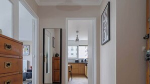 Un couloir avec un plancher en bois, une commode, un miroir et une cuisine visible à travers une porte ouverte.