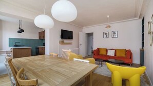 Een moderne leefruimte met een houten eettafel, gele stoelen, een rode bank en een keukenhoek.