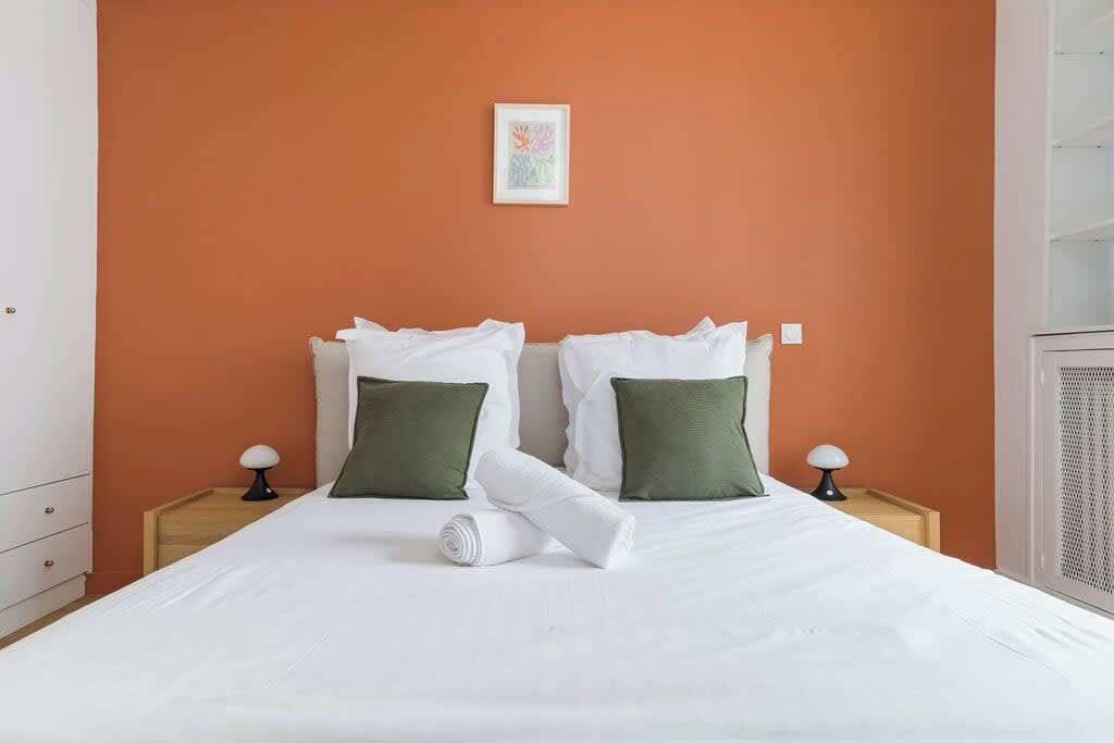 A hotel room with a bed, two green pillows, white bedding, a framed picture on the wall, and two bedside lamps.
