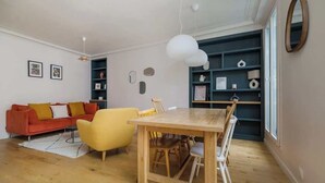 Een woonkamer met een houten eettafel, een rode bank, een gele fauteuil en een boekenplank.