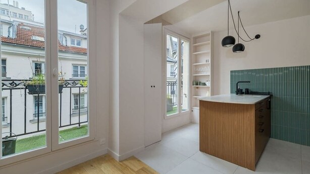 Een moderne keuken met een houten bar, witte kastjes en een uitzicht op de stad door grote ramen.